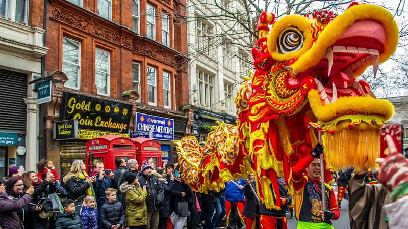 Colorful Chinese New Year dragon parade with lively dancers, spectators, and traditional costumes celebrating Lunar New Year festivities on a city street.