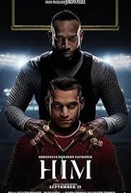 A man sitting confidently with a serious expression, wearing a dark sweater against a moody background.