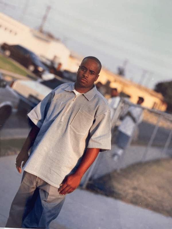 Men standing outdoors on an urban street, wearing casual clothing in a daytime setting.