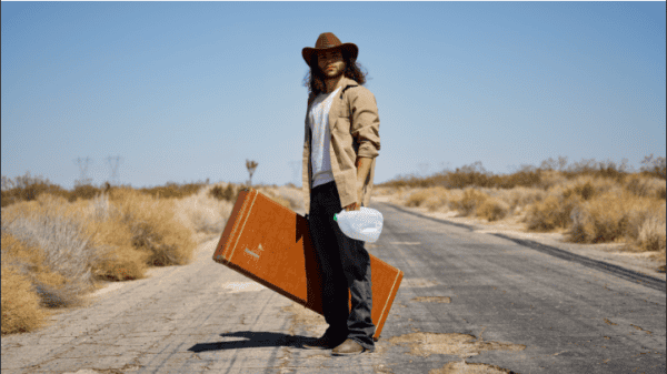 Long brown suitcase, traveler woman in desert, packing for journey, adventure travel, rugged landscape, solo travel, outdoor exploration, stylish travel outfit, solo female traveler, scenic desert road, travel essentials, nostalgic travel vibe.