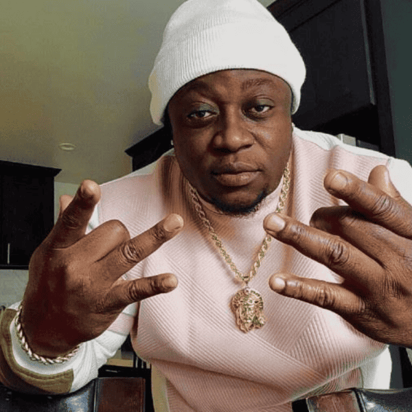 Diamond-encrusted jewelry, rapper in stylish pink outfit and white beanie showing hand gestures, luxury accessories, hip-hop artist in contemporary setting.