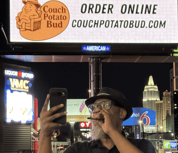 Couch potato bud logo on billboard with online ordering website couchpotatobud.com, night cityscape, Las Vegas neon lights, urban entertainment and nightlife scene, popular local corner bar, vibrant city life scene.